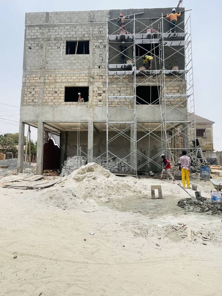 Steel tube scaffolding against a blockwork elevation, with workers rendering the upper floors.
