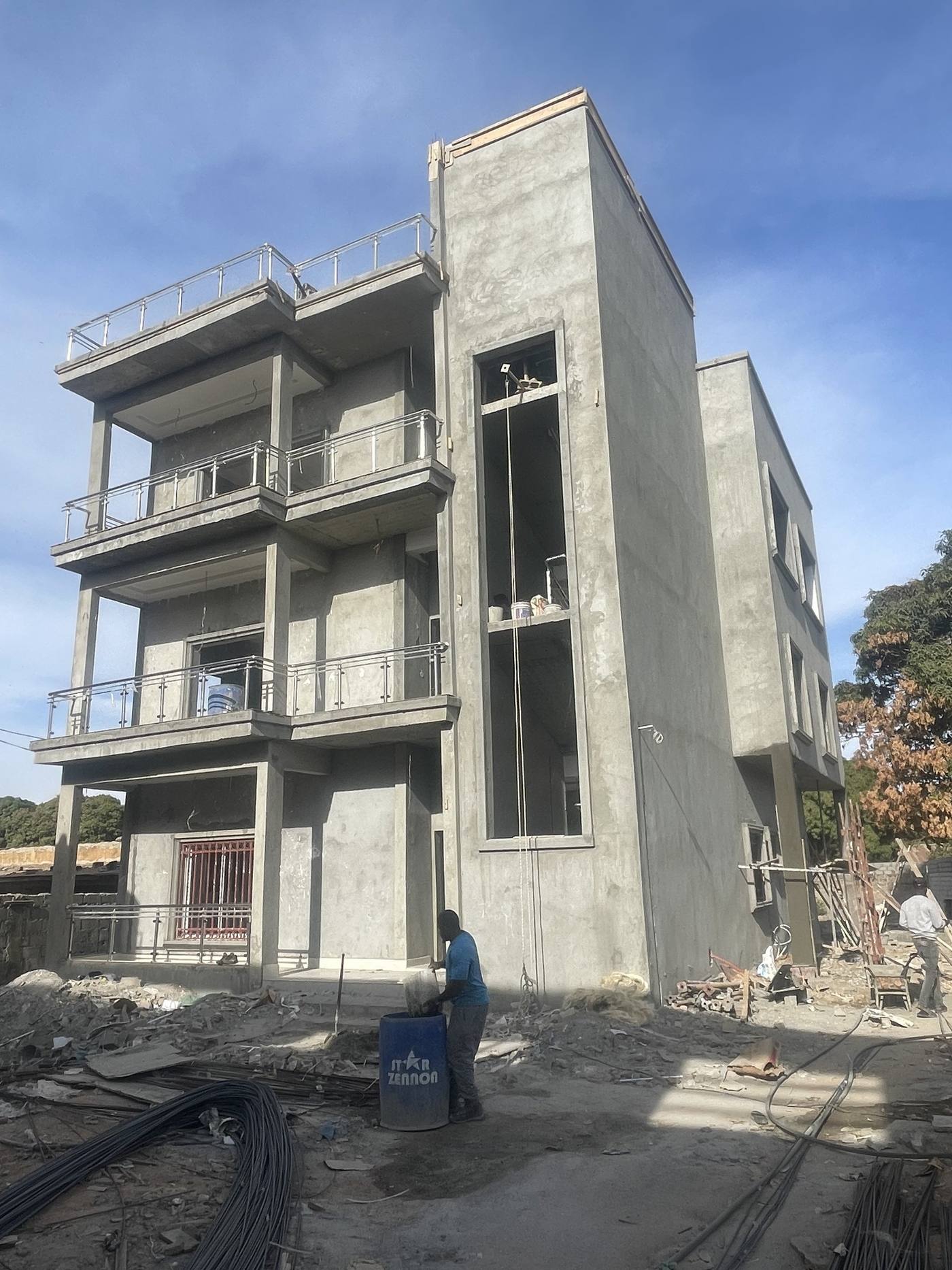 The Banjulinding structure at full height, its concrete frame and floor slabs cast and the walls rendered, with a balcony to each upper floor.