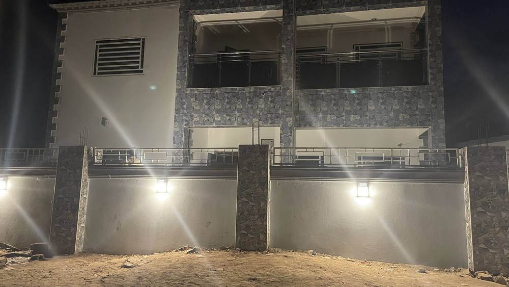 The front of the two-storey house at night, its stone-clad external walls lit from below.