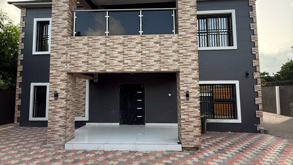 The front facade of the completed two-storey Kololi residence, with a stone-clad entrance bay rising through both floors.