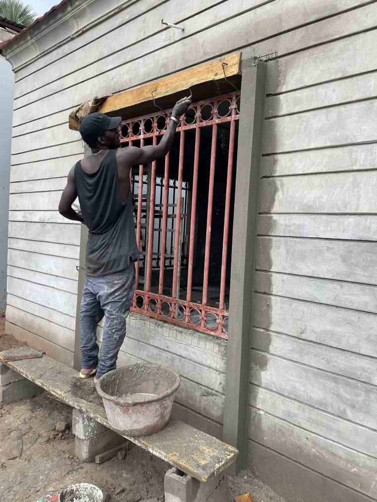A worker on a plank applying render around a window opening, the banded wall finish already run across the elevation.