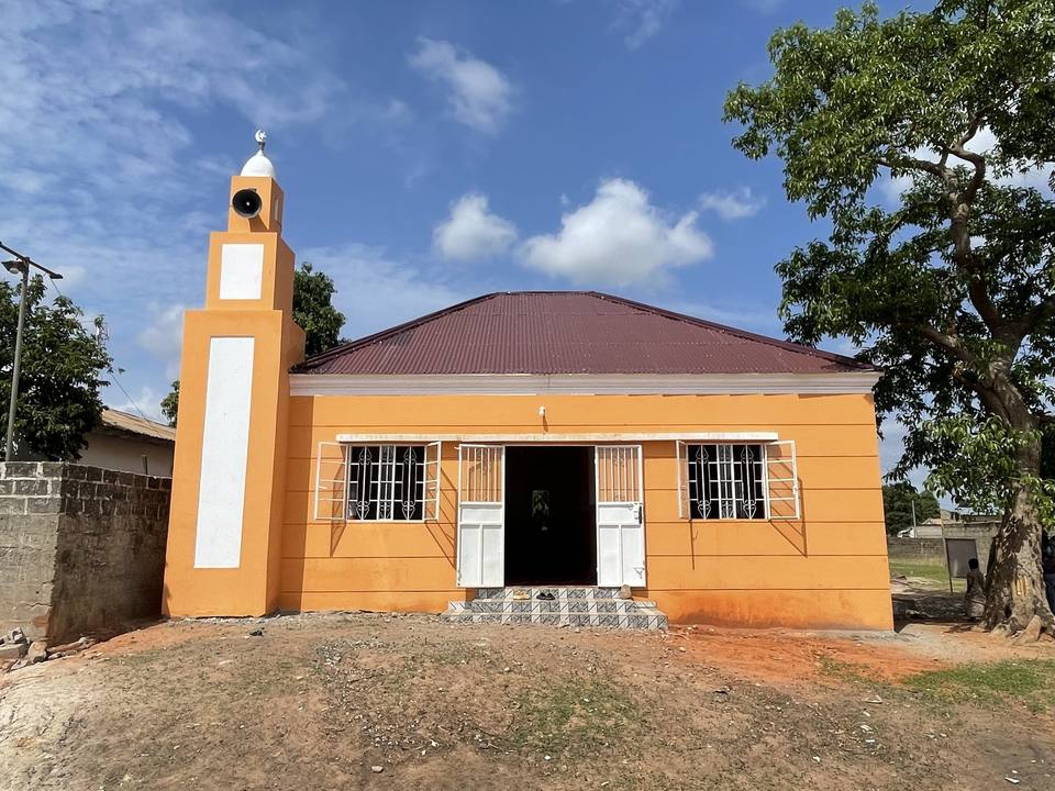 The completed exterior of Manduar Mosque, a single-storey prayer hall with a minaret rising at one corner.